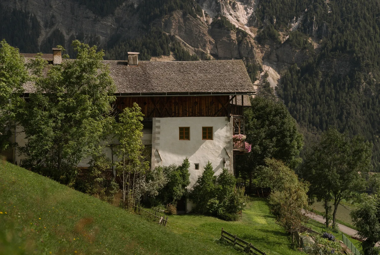 Tradizionale maso altoatesino con balcone di gerani davanti a fondale montano in estate, Funes-Luson