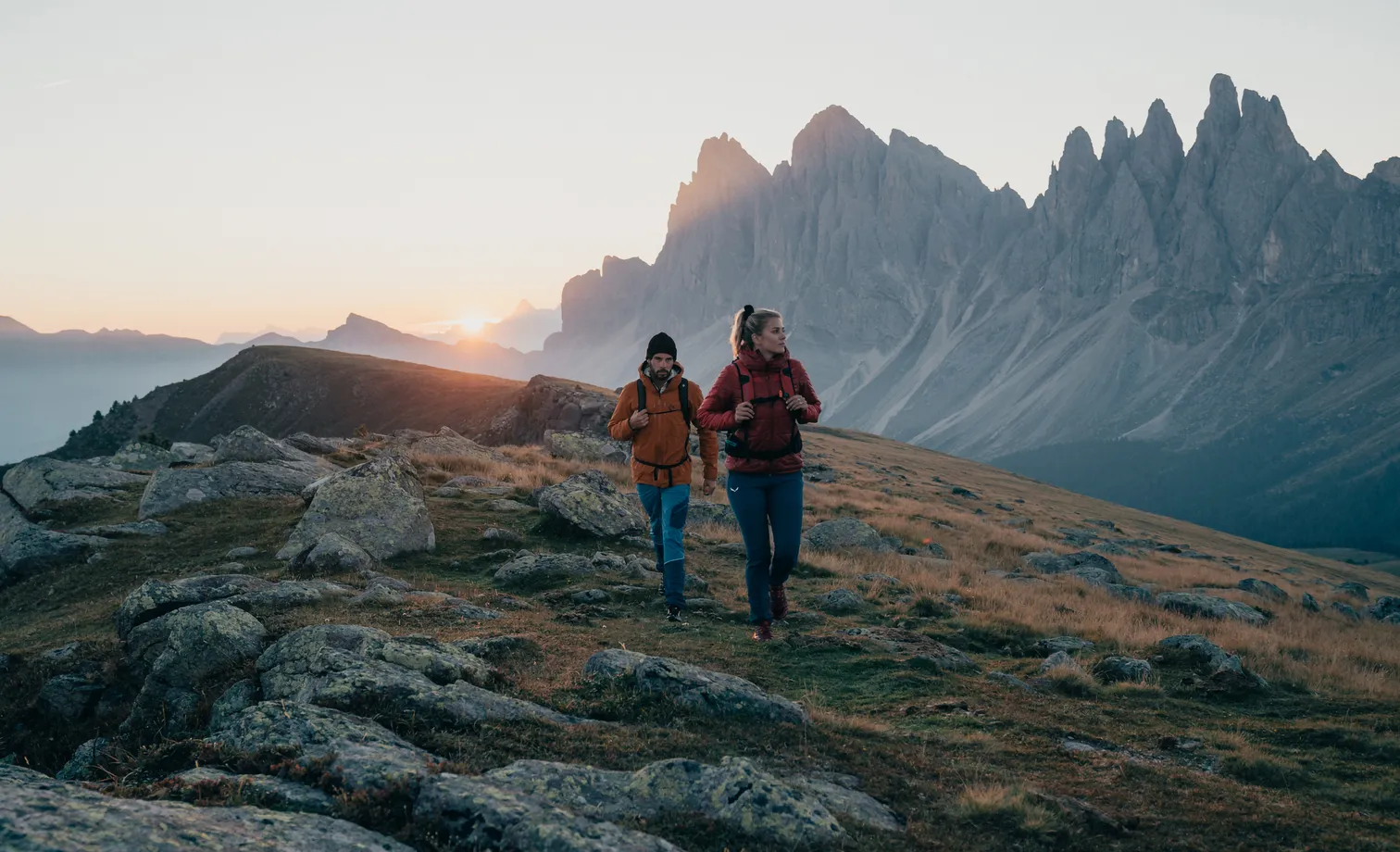 Herbstwanderung im Hochgebirge: Paar vor den Geislerspitzen auf dem Adolf-Munkel-Weg bei goldenem Sonnenuntergang