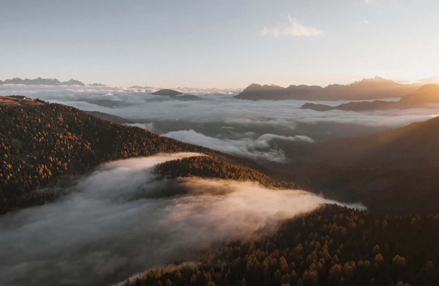Luftaufnahme: Goldenes Herbstlicht über Lärchenwäldern bei Lüsen, dichtes Nebelmeer füllt die Südtiroler Täler bei Sonnenaufgang