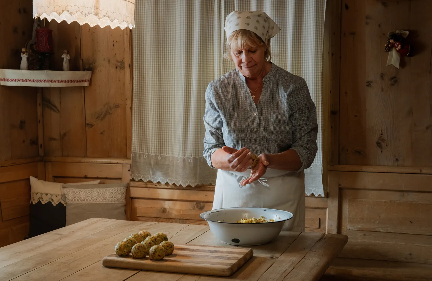 Bäuerin formt traditionelle Südtiroler Spinatknödel in rustikaler Holzstube in Villnöß