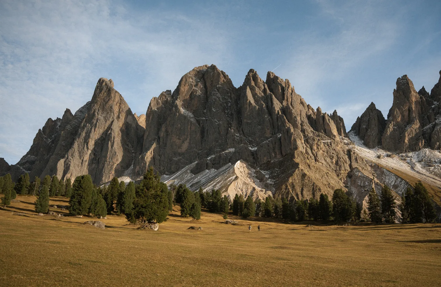 Autumnal alpine meadow with hikers in front of the rugged Geisler rock pinnacles in Villnöß valley, South Tyrol