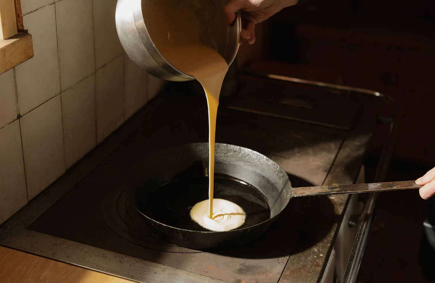 Kaiserschmarrn-Teig wird aus dem Topf in gusseiserne Pfanne auf altem Holzherd gegossen