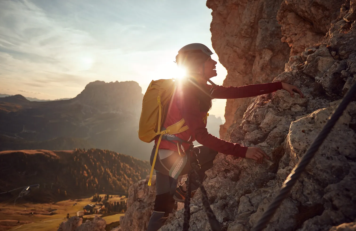 Female climber on the via ferrata of the Geisler group at sunrise with Dolomite panorama and golden larches