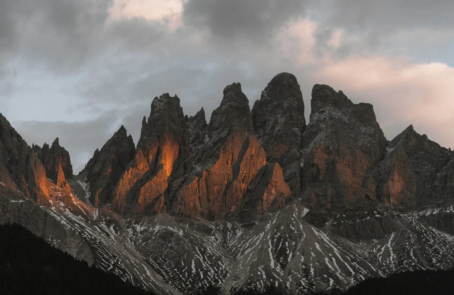 Alpenglühen an den Felstürmen der Geislergruppe bei Sonnenuntergang mit orange leuchtenden Dolomit-Wänden und Schneeresten an den Schutthalden
