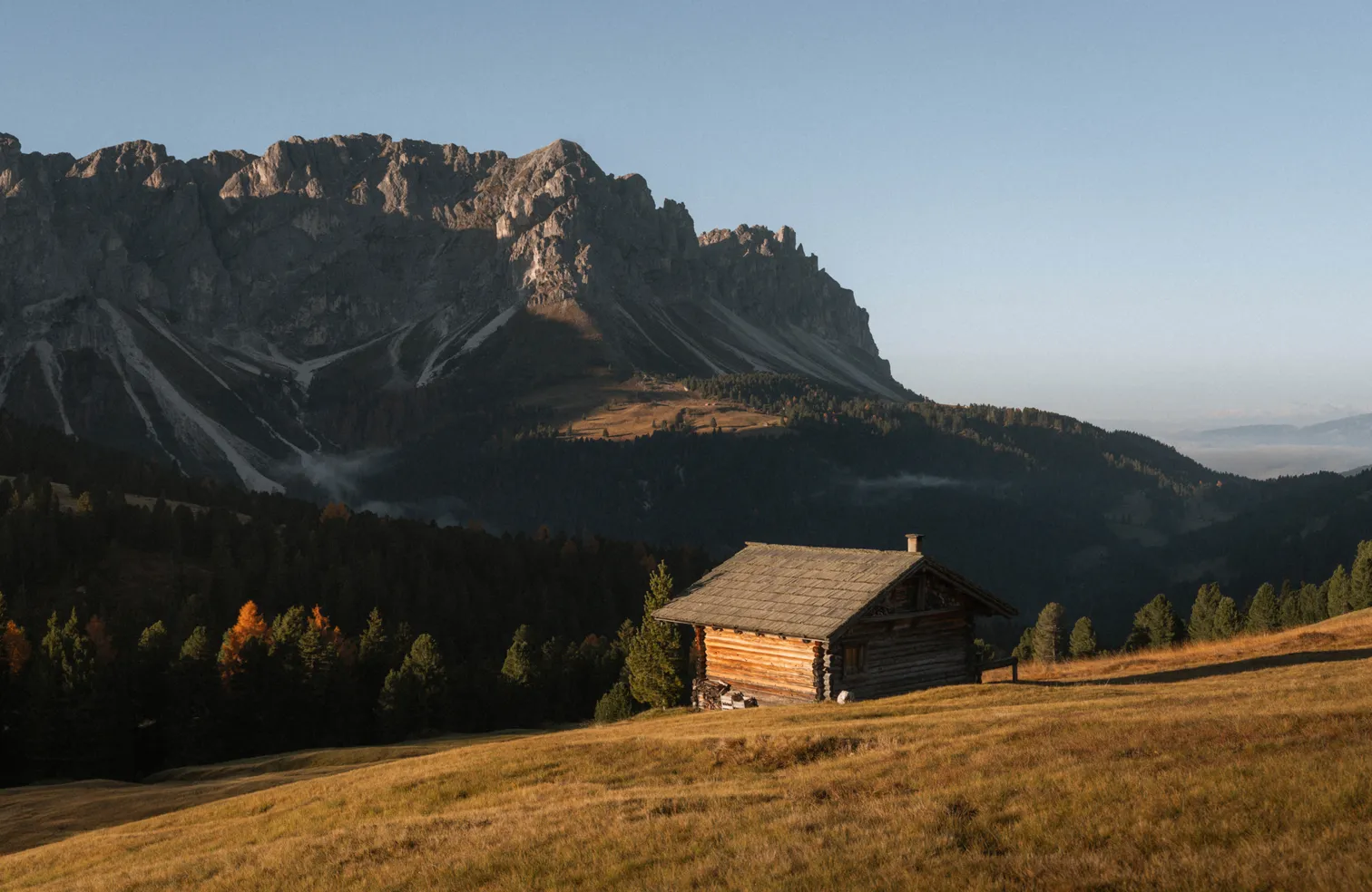 Holzhütte auf der Lüsner Alm im goldenen Herbstlicht vor der mächtigen Peitlerkofel-Nordwand – Odles Dolomiten Südtirol