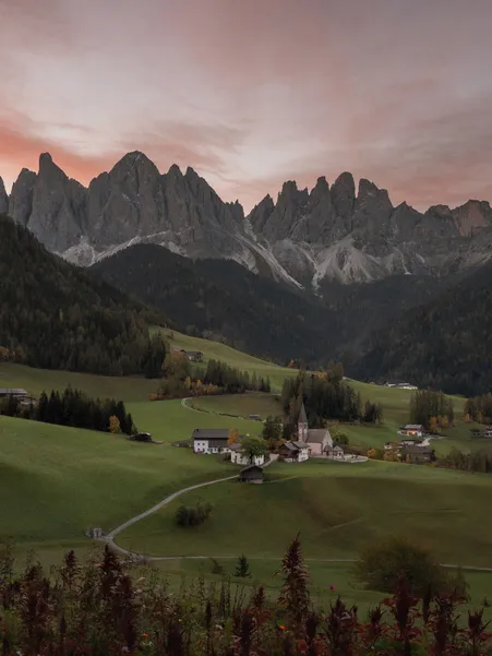 St. Magdalena in Villnöß bei Sonnenuntergang mit den Geisler-Spitzen der Dolomiten und herbstlichen Almwiesen