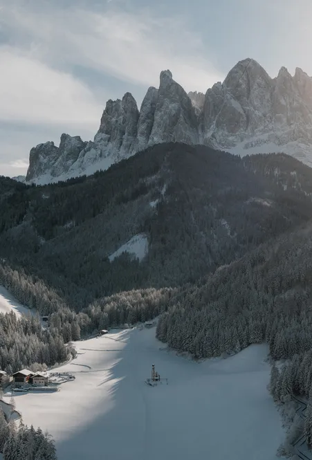 Winter Villnöß valley with snow-covered forests and the church of St. Magdalena in front of the Geisler Dolomites in sunlight
