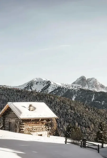 Snow-covered wooden hut above Luson with view of Peitlerkofel and coniferous forests in the South Tyrolean Dolomites