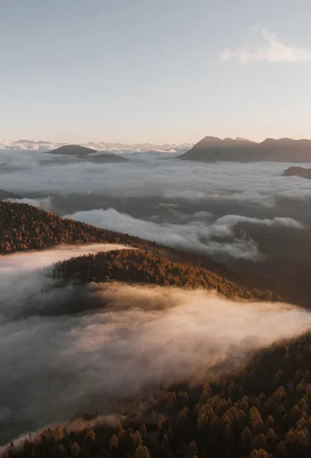 Autumnal sea of clouds over Luson valley at sunrise with forested mountain ridges and Dolomite peaks
