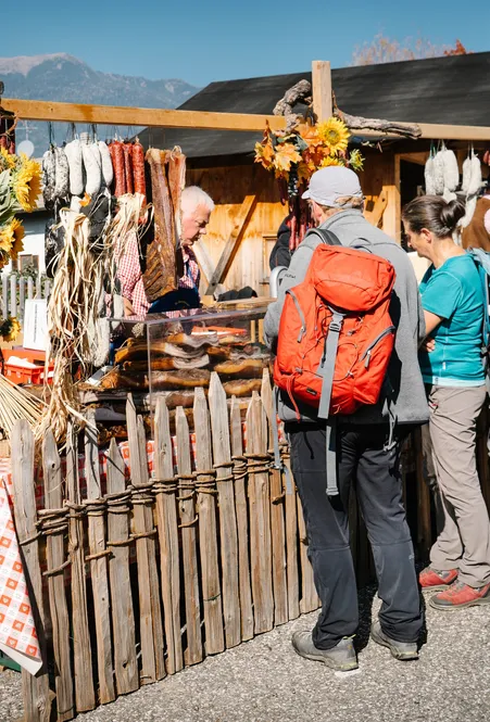 Marktstand mit aufgehängten Südtiroler Würsten und Speck auf einem Bauernmarkt in Villnöß Wanderer beim Einkaufen