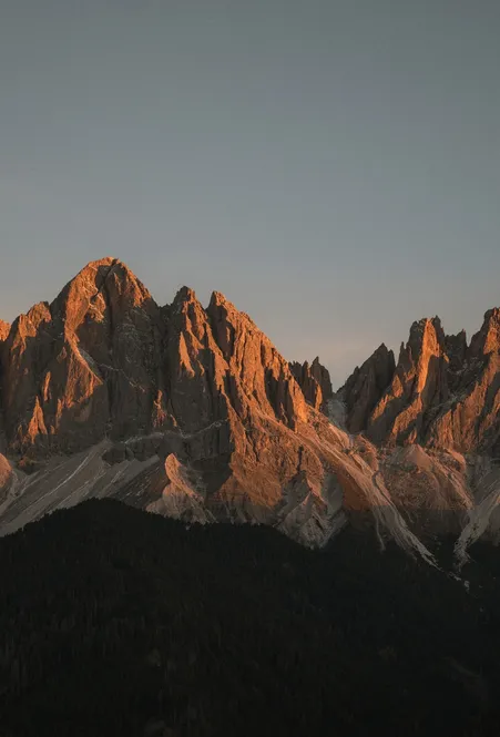 Alpenglow on the Geisler group – Odles rock pinnacles glow orange-red at sunset above forests near Villnöß