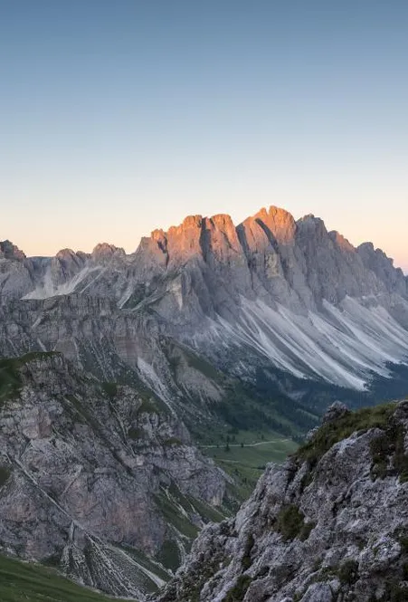Female climber on the Günther Messner trail with steel cable in rock, Geisler group at sunrise in the background
