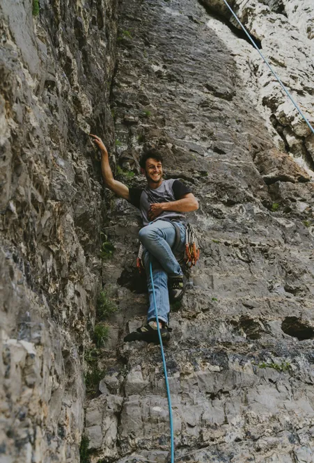 Young climber with harness and quickdraws smiles on rope in steep rock face