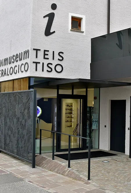 Moderner Eingang des Mineralienmuseums Teis Tiso mit Glasfront, beleuchteten Vitrinen und Touristeninformation-Symbol