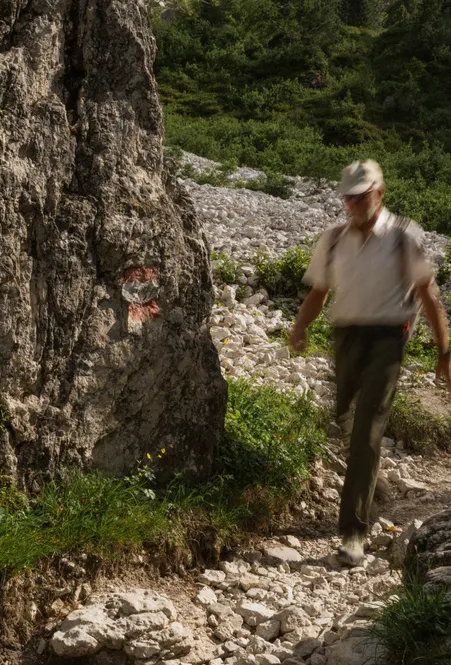 Escursionista con berretto cammina lungo sentiero roccioso segnalato sopra ghiaione nel gruppo delle Odle delle Dolomiti in estate