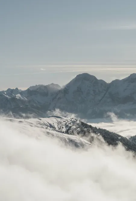Dolomiten-Gipfelpanorama über dichter Wolkendecke im Tal mit verschneiten Bergrücken aus dem Nebelmeer bei fahlem Winterlicht über Lüsen