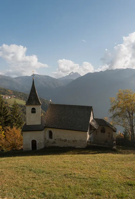 Historic chapel with shingle roof and bell tower on autumn meadow with view of mountain ranges near Luson in South Tyrol