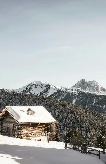 Snow-covered wooden hut above Luson with view of Peitlerkofel and coniferous forests in the South Tyrolean Dolomites