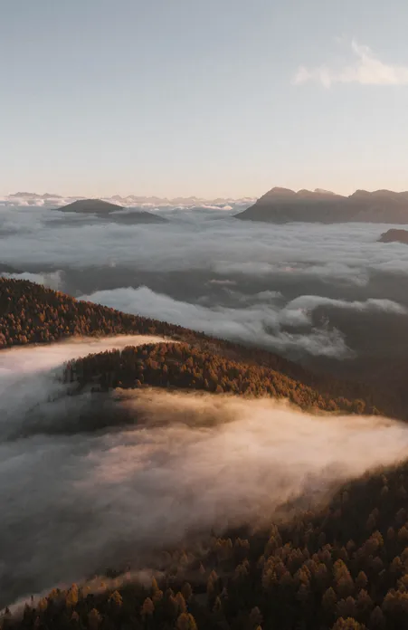 Autumnal sea of clouds over Luson valley at sunrise with forested mountain ridges and Dolomite peaks