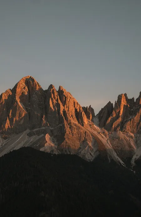 Alpenglühen auf den Geislerspitzen der Dolomiten bei Sonnenuntergang orange Felszacken über Wäldern bei Villnöß