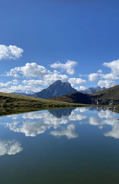 Lago di montagna sull'Alpe di Luson con perfetto riflesso delle Odle Dolomiti con cielo azzurro brillante a Funes Alto Adige