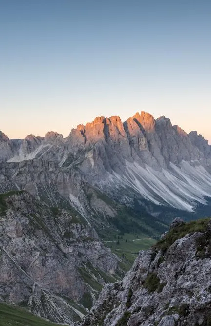 Arrampicatrice sul sentiero Günther Messner con cavo d'acciaio nella roccia, gruppo delle Odle all'alba sullo sfondo