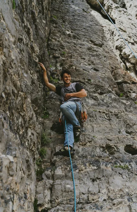 Giovane arrampicatore con imbracatura e rinvii sorride appeso alla corda in ripida parete rocciosa