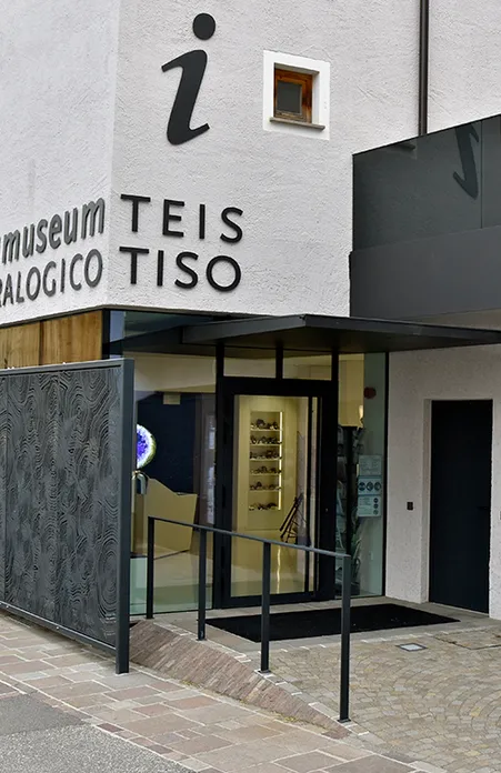 Moderner Eingang des Mineralienmuseums Teis Tiso mit Glasfront, beleuchteten Vitrinen und Touristeninformation-Symbol