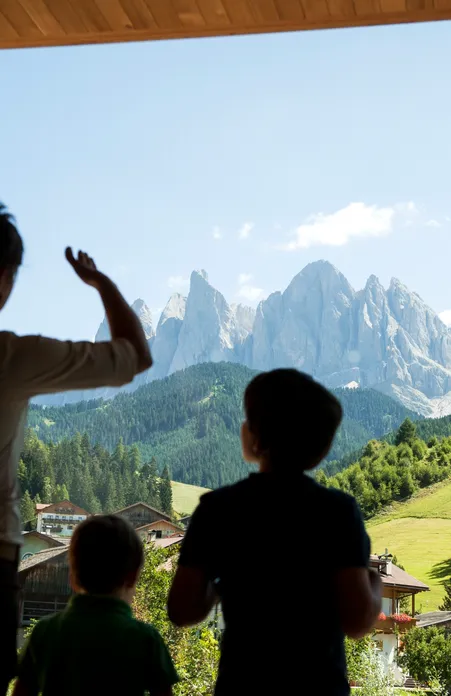 Family with children looks through panoramic window towards Geisler Dolomites and green meadows of Villnöß