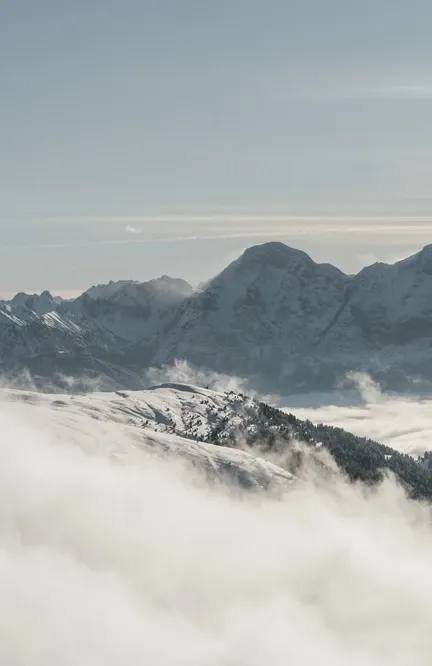 Panorama delle cime dolomitiche sopra denso strato di nuvole nella valle con creste montuose innevate che emergono dal mare di nebbia nella pallida luce invernale sopra Luson
