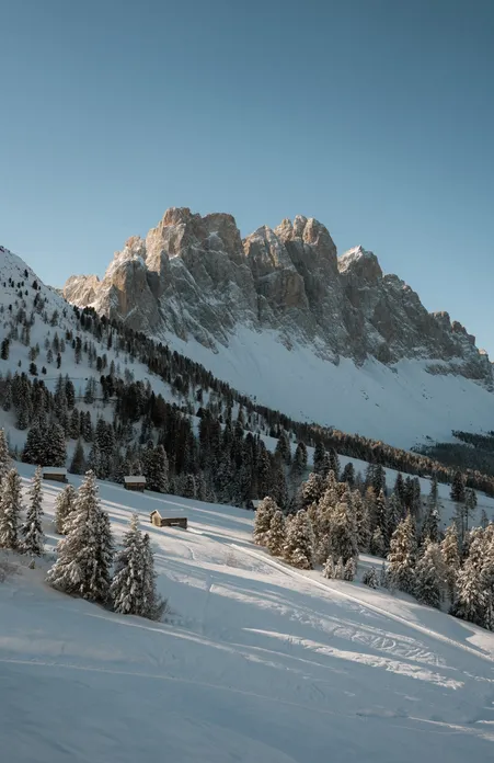 Deeply snow-covered alpine meadows and traditional mountain farms in front of the majestic Peitlerkofel in winter light