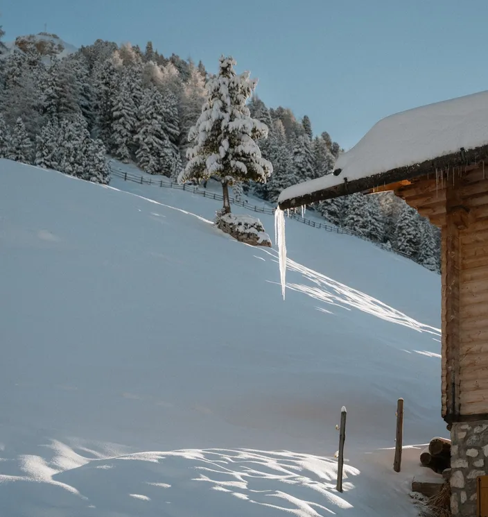 Verschneite Holzhütte mit Eiszapfen am Dach im Winter – Almhütte in der Geislergruppe Südtirol