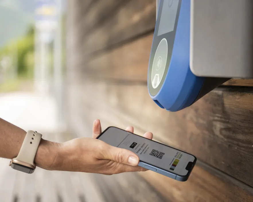 Mano tiene smartphone con biglietto digitale QR code presso lettore NFC alla fermata – convalida contactless in Alto Adige